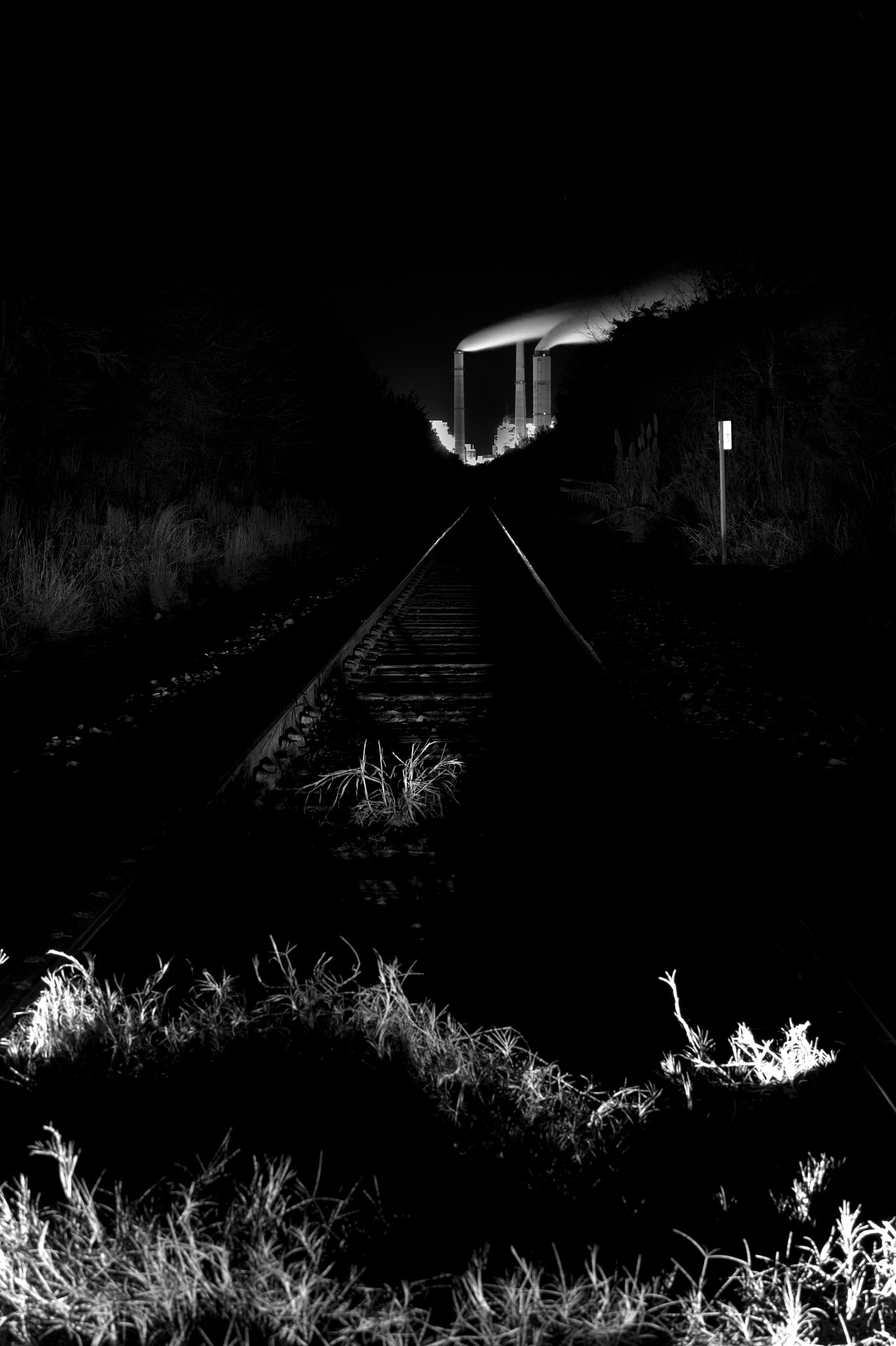 An industrial plant lit at night beyond rail tracks